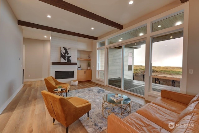 living room with a large fireplace, beamed ceiling, and light hardwood / wood-style flooring