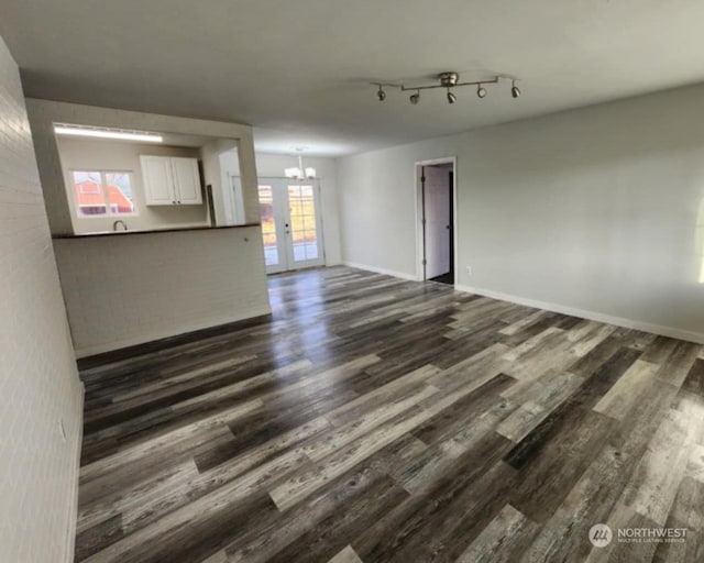 unfurnished living room with a healthy amount of sunlight, french doors, dark wood-type flooring, and a chandelier