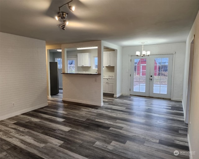 unfurnished living room featuring french doors, dark wood-type flooring, brick wall, and an inviting chandelier