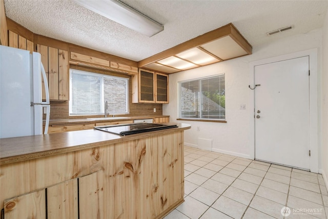 kitchen featuring a sink, light brown cabinets, freestanding refrigerator, light tile patterned floors, and visible vents