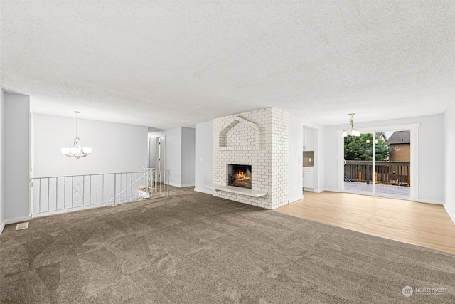 unfurnished living room with hardwood / wood-style flooring, a notable chandelier, a textured ceiling, and a brick fireplace