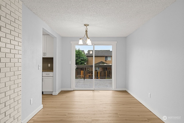 unfurnished dining area featuring light hardwood / wood-style floors, a textured ceiling, and an inviting chandelier