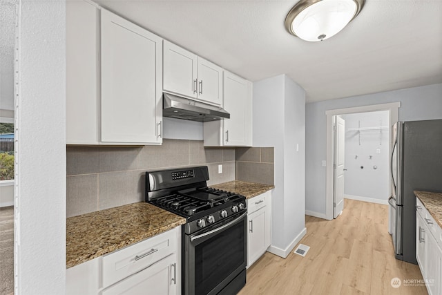 kitchen with dark stone countertops, white cabinetry, stainless steel appliances, and light hardwood / wood-style flooring