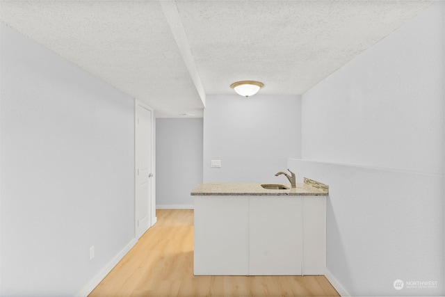 bar featuring sink, white cabinets, light hardwood / wood-style floors, and a textured ceiling