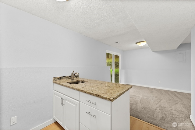 kitchen with light stone countertops, sink, a textured ceiling, light carpet, and white cabinets