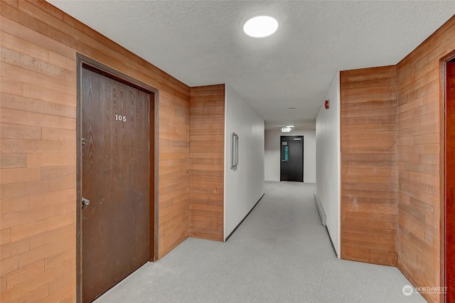 hall featuring a textured ceiling, light colored carpet, and wood walls