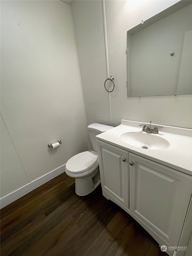 half bathroom featuring baseboards, vanity, toilet, and wood finished floors