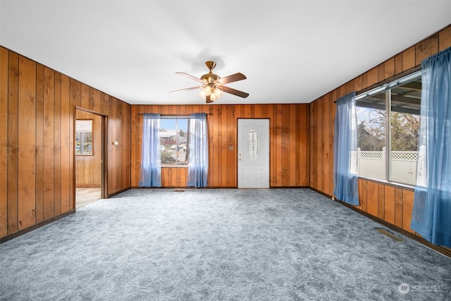 spare room featuring wooden walls, carpet flooring, ceiling fan, and a wealth of natural light