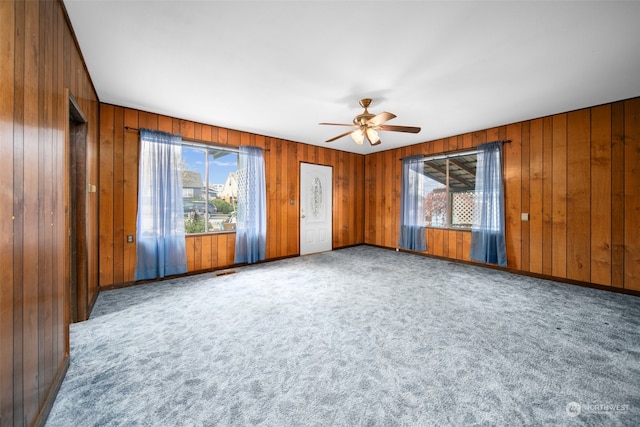 carpeted empty room featuring wooden walls, ceiling fan, and a healthy amount of sunlight