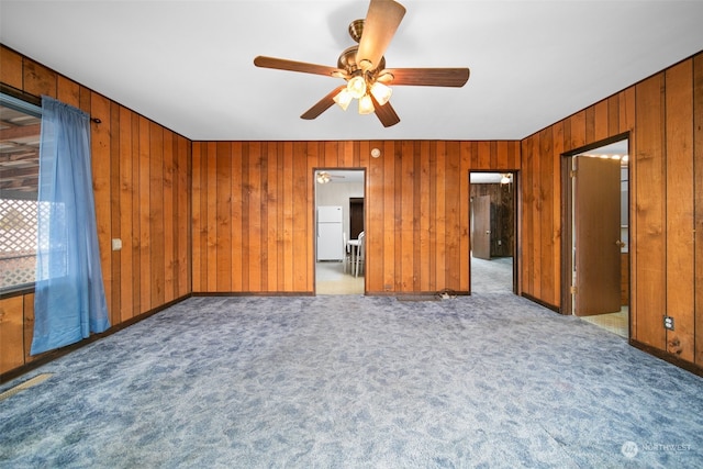 unfurnished bedroom featuring carpet, wood walls, and ceiling fan