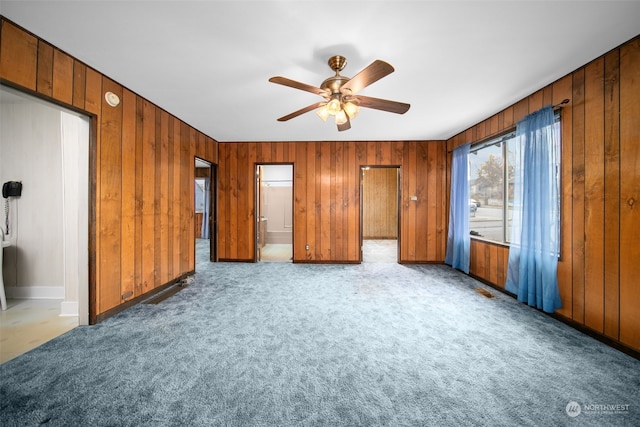 unfurnished bedroom featuring light carpet, ensuite bath, ceiling fan, and wood walls