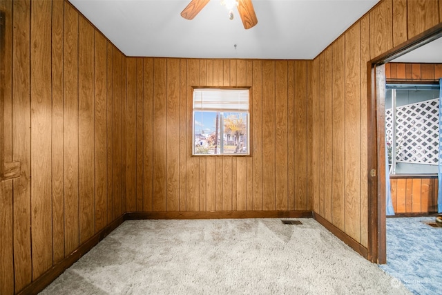 carpeted spare room with plenty of natural light, ceiling fan, and wooden walls