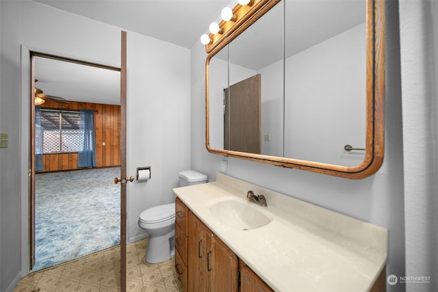 bathroom featuring ceiling fan, toilet, vanity, and wooden walls