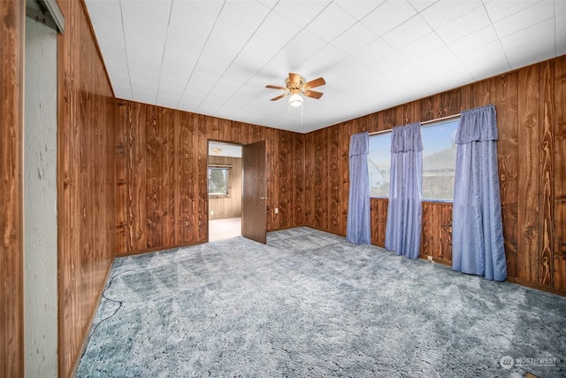 unfurnished room with wood walls, carpet floors, and ceiling fan