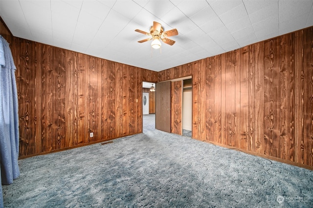 empty room featuring carpet floors, ceiling fan, and wooden walls