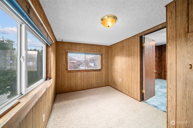 carpeted empty room with wooden walls and a textured ceiling