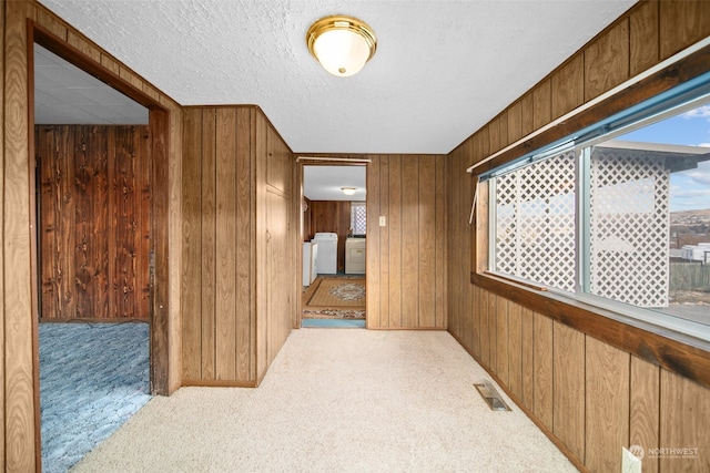 hall featuring a textured ceiling, light colored carpet, washer and clothes dryer, and wooden walls