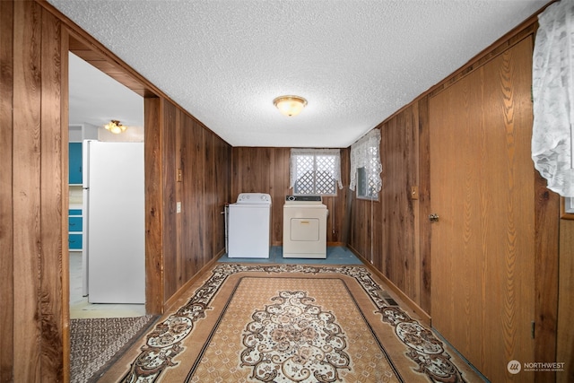 washroom featuring a textured ceiling, washer and clothes dryer, and wood walls