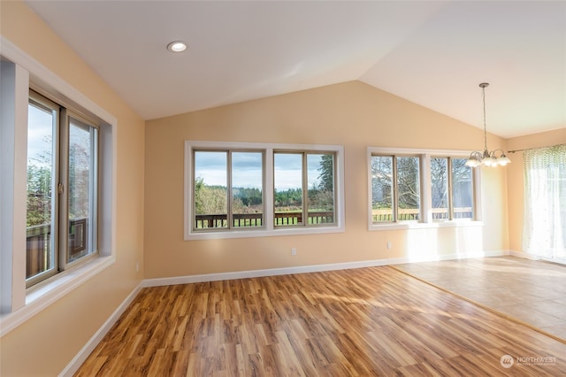 empty room featuring lofted ceiling, hardwood / wood-style flooring, a wealth of natural light, and a notable chandelier