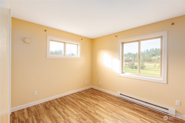 empty room with a healthy amount of sunlight, light hardwood / wood-style floors, and baseboard heating