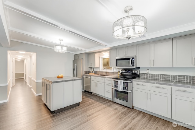 kitchen featuring sink, appliances with stainless steel finishes, decorative light fixtures, a kitchen island, and light wood-type flooring