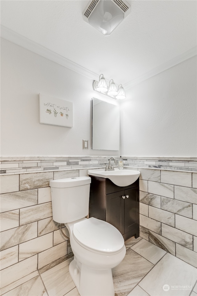 bathroom featuring toilet, vanity, tile walls, and ornamental molding