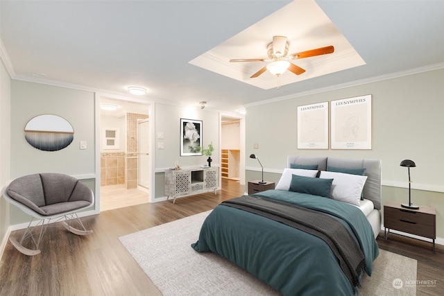 bedroom with a raised ceiling, crown molding, ceiling fan, connected bathroom, and wood-type flooring