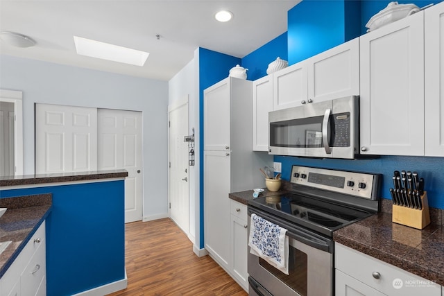 kitchen featuring white cabinets, hardwood / wood-style flooring, appliances with stainless steel finishes, and a skylight