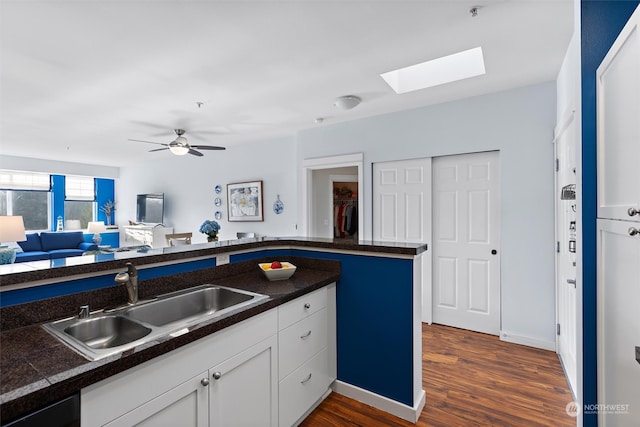 kitchen with white cabinets, sink, a skylight, ceiling fan, and dark hardwood / wood-style flooring