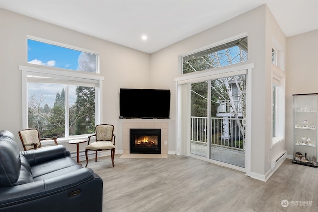 living room featuring light wood-type flooring, a fireplace, a towering ceiling, and a baseboard heating unit