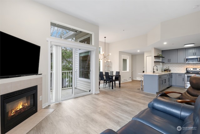 living room with a tiled fireplace, sink, a chandelier, and light wood-type flooring