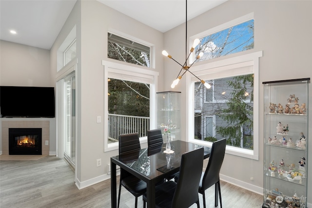 dining area with hardwood / wood-style floors, an inviting chandelier, a wealth of natural light, and a tiled fireplace