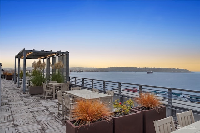 patio terrace at dusk featuring a water view and a pergola