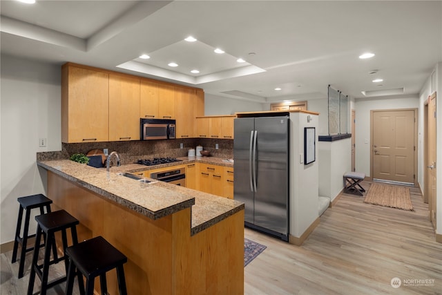 kitchen with light brown cabinetry, light hardwood / wood-style flooring, appliances with stainless steel finishes, and a tray ceiling