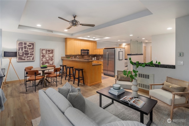 living room with radiator heating unit, light wood-type flooring, a tray ceiling, and ceiling fan