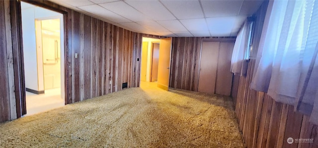 interior space featuring wood walls, a drop ceiling, and carpet floors