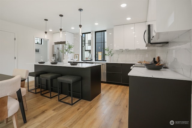 kitchen with white cabinetry, a center island, hanging light fixtures, stainless steel appliances, and light hardwood / wood-style flooring