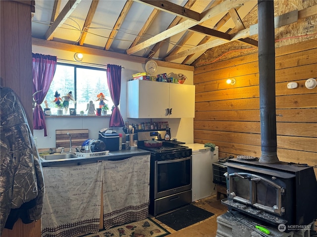 kitchen featuring a wood stove, white cabinets, sink, vaulted ceiling with beams, and black range with electric cooktop