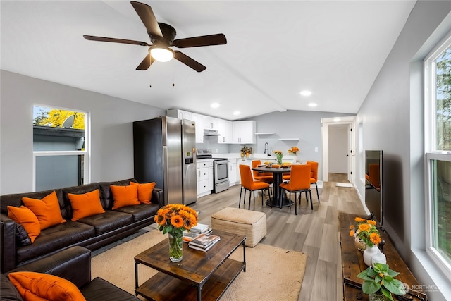 living room with light wood-type flooring, vaulted ceiling, ceiling fan, and sink