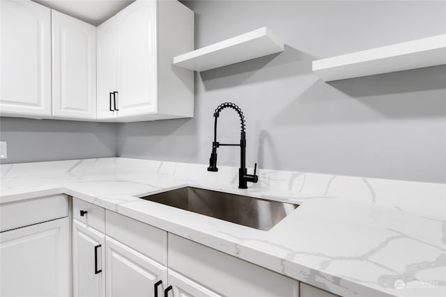 kitchen featuring light stone countertops, white cabinetry, and sink