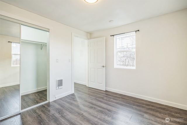 unfurnished bedroom featuring heating unit, dark wood-type flooring, and a closet