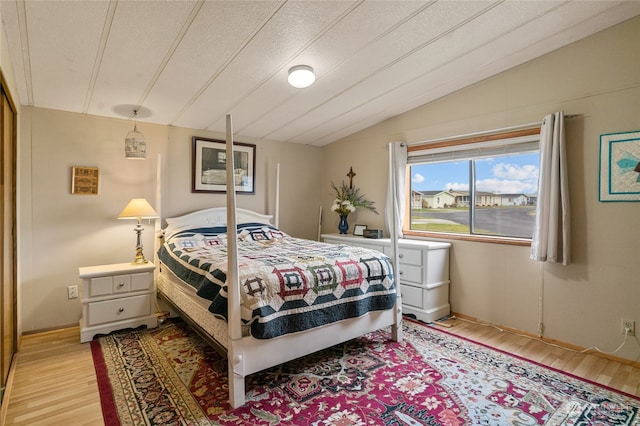 bedroom featuring light hardwood / wood-style floors, a textured ceiling, and vaulted ceiling