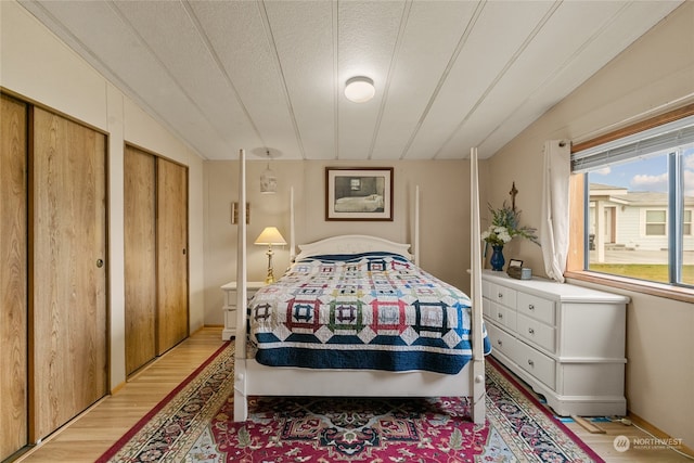 bedroom with hardwood / wood-style floors, a textured ceiling, vaulted ceiling, and multiple closets