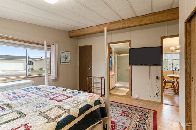 bedroom with beam ceiling, light hardwood / wood-style flooring, and ensuite bath