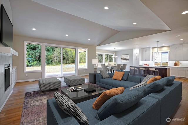 living room with a tile fireplace, light wood-type flooring, vaulted ceiling, and sink