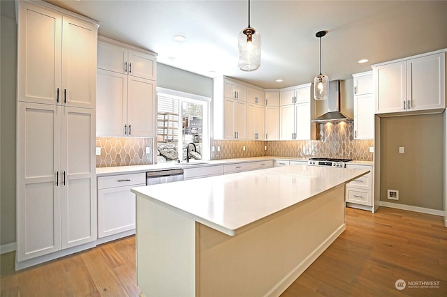 kitchen with sink, wall chimney exhaust hood, a kitchen island, pendant lighting, and white cabinets