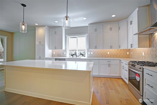 kitchen with appliances with stainless steel finishes, wall chimney exhaust hood, white cabinets, a kitchen island, and hanging light fixtures