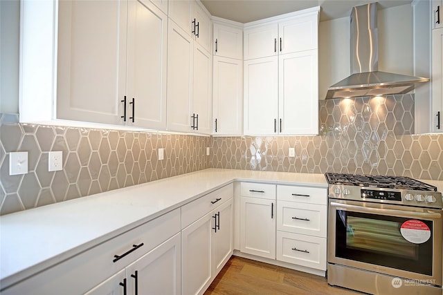 kitchen with backsplash, wall chimney range hood, light hardwood / wood-style flooring, stainless steel gas range, and white cabinetry