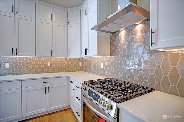 kitchen with high end stove, backsplash, white cabinetry, and wall chimney range hood