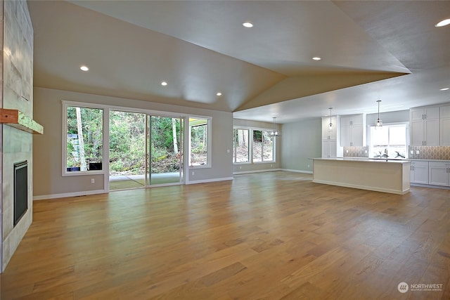 unfurnished living room with sink, light wood-type flooring, a fireplace, and vaulted ceiling